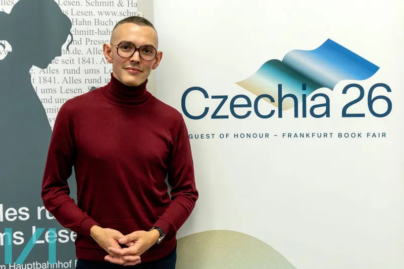 Vratislav Maňák - mladý muž v roláku stojící před bannerem Czechia 26.