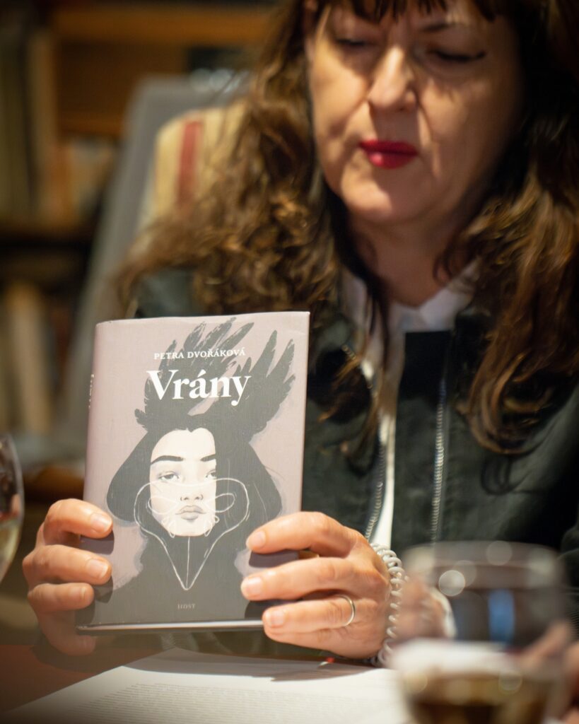 Překladatelka Hana Hadas na literární debatě v Rezidenci Café Kaprál, držící knihu Vrány od Petry Dvořákové